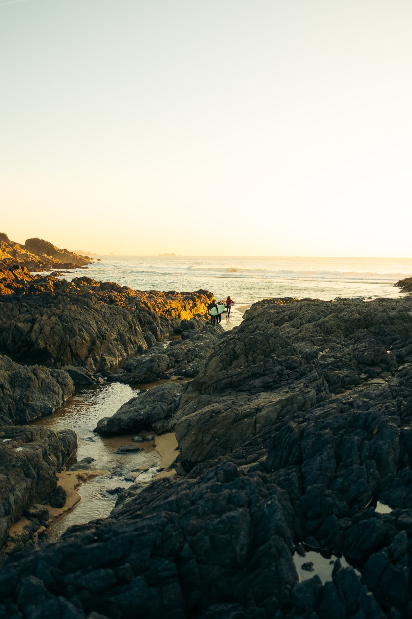 Côte rocheuse du Finistère au coucher du soleil avec surfeurs